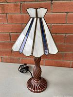 Full view of vintage stained glass table lamp showing twisted dark wood base and scalloped stained glass shade with white and blue panels.
