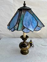 Full view of vintage stained glass table lamp showing petal-shaped blue and green glass shade and brass base.