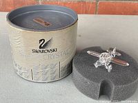 Full view of the vintage Swarovski crystal airplane displayed on foam insert next to its original cylindrical packaging tube labeled Swarovski Crystal.