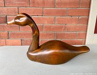 Wooden duck decoy showing the right side view against a red brick wall background.