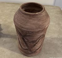 Brown pottery vase pot on beige surface showing unglazed texture and geometric design details