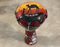Top view image of 9-inch hand crafted Tunisian drum showing camel, guide, and cow artwork with 'Tunisie' imprint on drumhead.