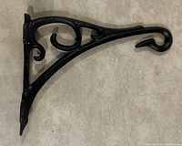 Black Romanesque plant bracket photographed on a neutral surface, showing curved, scroll and decorative details in the wrought style panel.