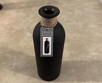 Front view of black chalkboard vase with rope detail wrapped near the neck and a tag illustrating its use for chalk writing.