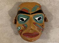 Front view of the hand painted cedar totem mask showing colors, design and facial features.