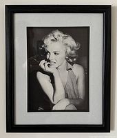 Black and white photograph of Marilyn Monroe framed in a black wood frame with a reverse step pattern and glass mounted, displayed against a neutral wall.