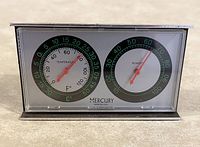 Vintage Mercury weather station displaying thermometer and humidity gauges with black and green dial markings and red needles inside a silver rectangular frame.