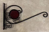 Image of a black metal wall hanging bracket with curled design and a central circular red piece, suitable for hanging plants or decorations.