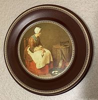 Front of the round metal plaque featuring reproduction of The Kitchen Maid painting by Jean Baptiste Simeon Chardin with detailed border.