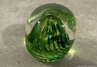 Close-up photo of a green glass paperweight with a unique interior mountain shape design visible inside the glass.