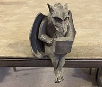 Gargoyle figurine sitting at the edge of a table with a laptop on its lap, showing front and side views