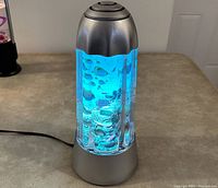 Vintage motion fish lamp turned on, casting blue light, showing fish and aquatic shapes inside.