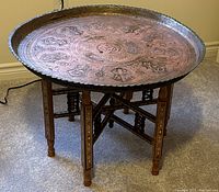 Overall view of the brass tray set on the mosaic folding wooden base showing the tray's engraving and base details.