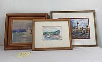 Three framed watercolor paintings featuring coastal and landscape scenes shown together on a white wall
