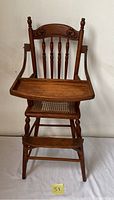 Front view of the antique wooden child's highchair with attached tray showing detailed spindle back and caned seat.