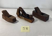 Three antique wooden hand planes arranged on a white surface with a small note showing number 58.