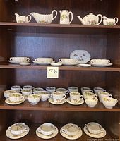 Full view of multiple shelves displaying the pottery set including teapot, gravy boat, creamers, cups, saucers, and small serving tray, all with a floral pattern on cream colored ceramic.