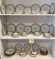 Full view of the Noritake Goldston china set displayed on white shelves showing multiple plates, bowls, tea cups with saucers, gravy boat, and sugar bowl.