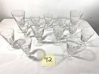 4 wine glasses and 9 smaller cordial glasses arranged on a white surface with lot number 42 in front