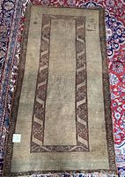 Full view of the rectangular Turkish tribal rug showing the geometric reddish-brown border and muted beige center field with scattered tribal motifs.