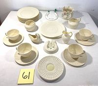 Full display of lot items including porcelain teacups with saucers, sugar bowl, creamer, small floral vase, swan pitcher, horseshoe decoration, and commemorative Christmas plate.