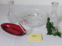 Full lot overview showing two cut crystal decanters, large cut crystal bowl, red glass swan candy dish, and green glass lady figurine sculpture