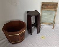 Three vintage wooden domestic items: wooden framed metal washboard, octagonal wooden stand, and octagonal barrel container, arranged on white cloth surface.