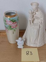 Photo showing flower vase with pink rose design, small angel figure, and Mother of Mary figure.