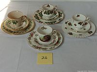 Four sets of teacups, saucers, and plates displayed together showing varying holiday and floral patterns with gold trim.