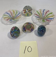 Overview of the full lot displaying two ribbon and lace style candy dishes and three Murano millefiori paperweights including round and oval shapes.