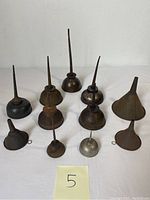 Ten vintage metal oil cans arranged standing upright on white surface.