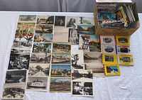 Wide overhead view of variety of vintage postcards spread out, plus box containing photo books and more postcards.