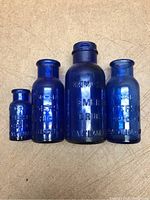 Four blue cobalt antique medicine bottles arranged from smallest to largest on brown textured surface.