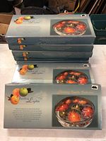 Nine stacked unopened boxes of Garden Lights Floating Candle Collection showing floating leaf-shaped candles in autumn colors.