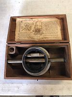 Top-down view of antique brass farm level set inside wooden box with original instruction sheet above it.