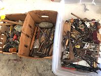 Photo showing two large containers full of antique tools including clamps, pliers, and miscellaneous hand tools, some metal and some wooden handled.