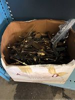 Box filled with assorted used flatware items including spoons, forks, and knives in various conditions.