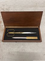 Photo of the open wooden box displaying the scissors and mail opener inside with gold and silver tones.