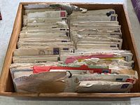 View of a wooden box filled with a large quantity of yellowed, aged letters and envelopes upright and packed tightly after decades of storage.
