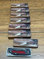 Seven boxed Bandit II knives laid out with one knife removed from the box showing handle and chain