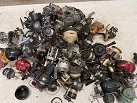 Top-down view of large pile of fishing reels tangled and overlapping, showing variety of colors and wear.