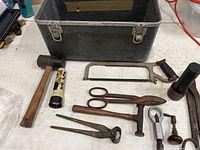 Photo showing the toolbox, mallet, saw, scissors, tin snips, hammer, and two flashlights with oxidation visible.
