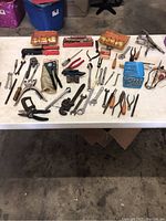 Wide view of the assorted vintage hand tools spread on white table, showing pliers, wrenches, screwdrivers, files, and other tools.