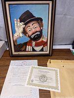 Framed print of clown character by Red Skelton along with certificate and paperwork spread on table
