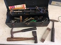 Open toolbox showing assortment of hand tools inside and some tools placed in front on table.
