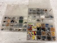 Top view of two plastic organizer boxes, showing multiple compartments filled with various hardware items including screws, nuts, washers, wall anchors and wooden dowels.