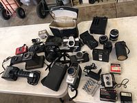 Wide layout of the vintage camera lot showing multiple cameras, lens, cases and accessories on a white table.