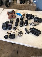 Overview of all items laid out on white table including cameras, lenses, flashes, light meter, and accessories