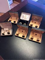 Full view of six pairs of cufflinks in their original boxes, showing variety and packaging condition.