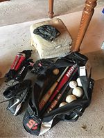 Full view of the set including baseball bats, gloves, cleats, shin guards, baseballs, and black sports bag placed on floor.